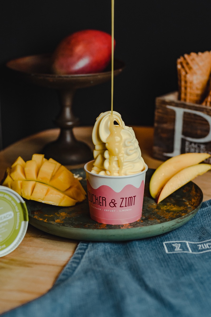 Softeis im Becher mit Mango und Bananen auf einem Holzbrett