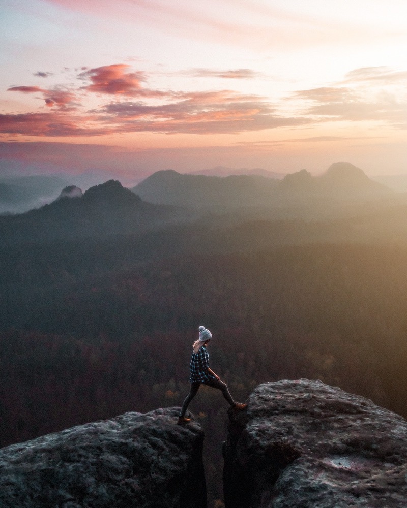 Eine Person steht auf einem Felsen über einem Tal im Abendrot