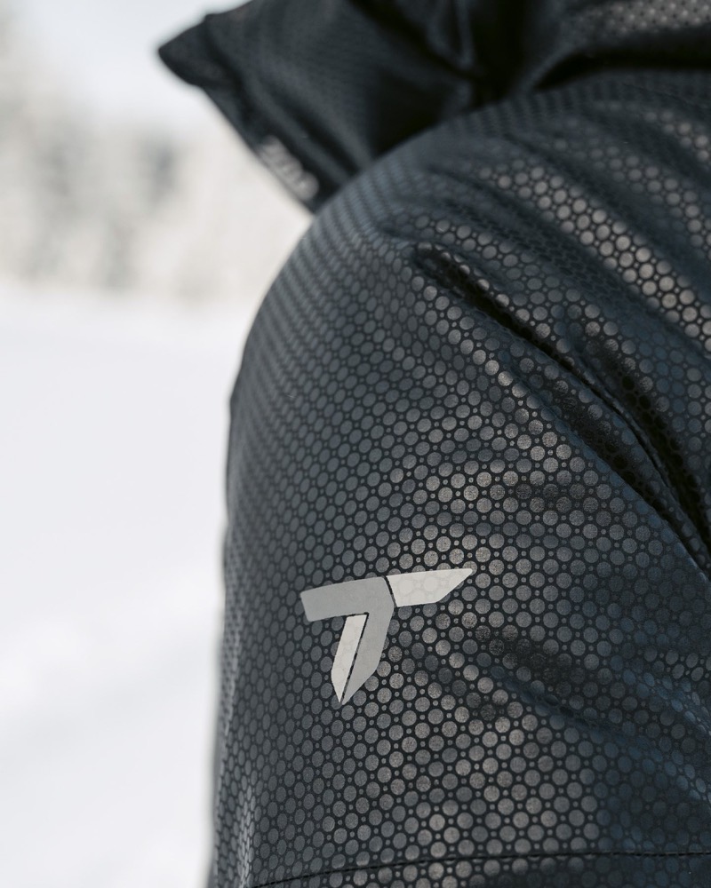 Nahaufnahme einer dunklen Funktionsjacke vor verschneiter Landschaft