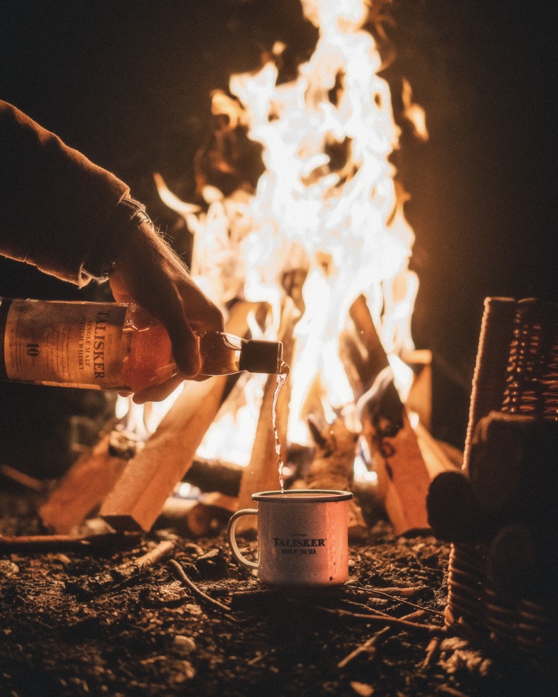 Lagerfeuer mit Funken in der Dunkelheit, daneben ein Kochtopf