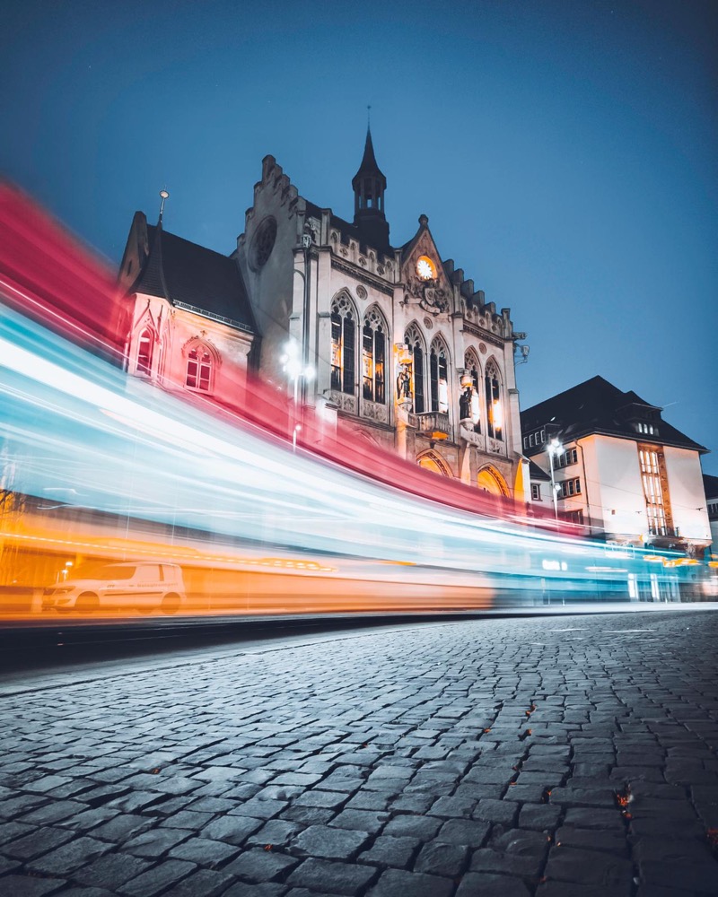 Lichtspuren von Straßenbahnen vor einem beleuchteten historischen Gebäude am Abend